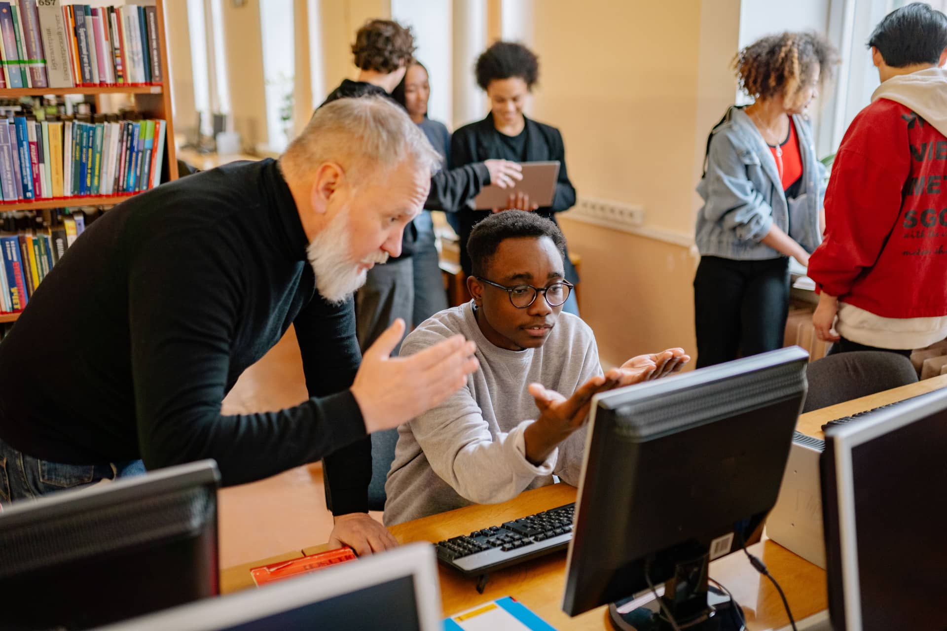 A tutor leaning in to help a student at a workstation